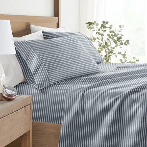 A neatly made bed features blue and white striped bedding, accompanied by a bedside table with a white lamp, a small succulent plant, and a clock.