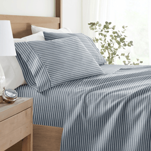 A neatly made bed features blue and white striped bedding, accompanied by a bedside table with a white lamp, a small succulent plant, and a clock.