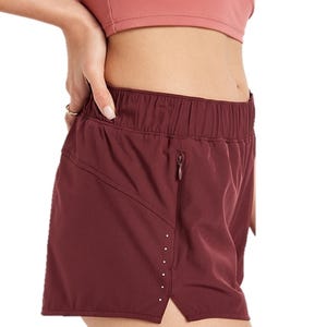 A person wearing maroon athletic shorts with an elastic waistband and a side zipper pocket, paired with a dark pink sports bra.