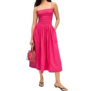 A woman wears a bright pink midi sundress with a smocked bodice and thin straps, paired with black sandals. She carries a pink textured handbag.