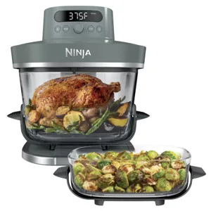 A Ninja cooking appliance, likely a multi-purpose air fryer or oven, is shown cooking a roasted chicken with vegetables. Nearby, a dish of roasted Brussels sprouts is displayed.