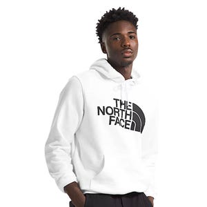 A man wears a white The North Face hoodie with a black logo, paired with dark pants.