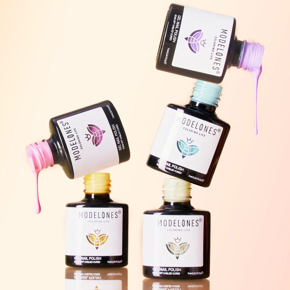 Four bottles of Modelones gel nail polish, in various colors (pink, purple, blue, and yellow), are stacked in a playful arrangement, with some polish dripping from the top bottles.