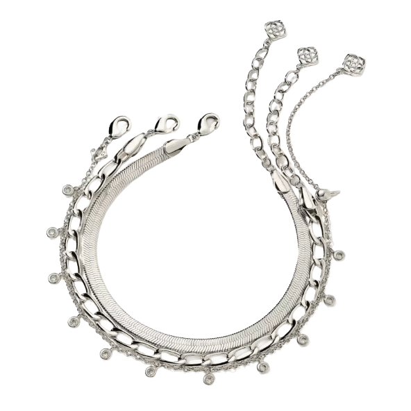 A silver necklace featuring multiple chain styles, including snake, curb, and cable chains, is adorned with small circular charms and delicate links terminating in geometric motifs.