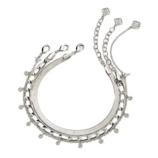 A silver necklace featuring multiple chain styles, including snake, curb, and cable chains, is adorned with small circular charms and delicate links terminating in geometric motifs.