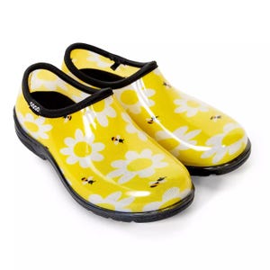 Yellow garden clogs with black trim, featuring a pattern of white daisies and small bees. They have a slip-on design and black soles.
