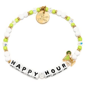 The Little Words Project Happy Hour Bracelet features white and light green beads with a gold charm displaying the phrase \“HAPPY HOUR.\“ It includes a small cocktail charm and gold accents, adding a playful touch to the design.