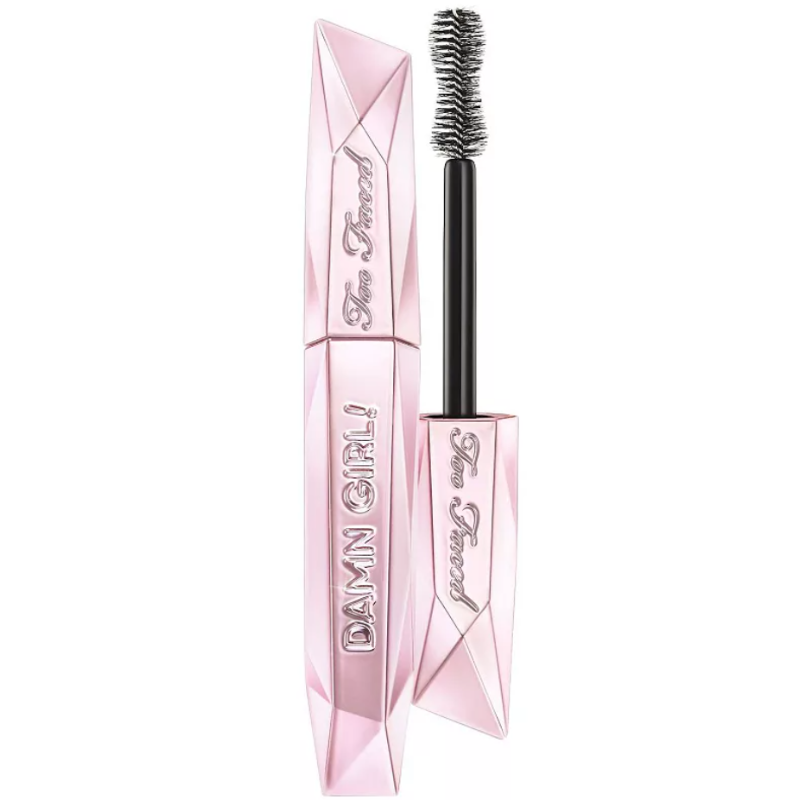 Too Faced Damn Girl! 24-Hour Mascara features a pink, diamond-shaped tube with a large hourglass brush for volumizing lashes. The packaging is embossed with the brand name and product name.