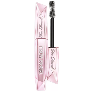 Too Faced Damn Girl! 24-Hour Mascara features a pink, diamond-shaped tube with a large hourglass brush for volumizing lashes. The packaging is embossed with the brand name and product name.