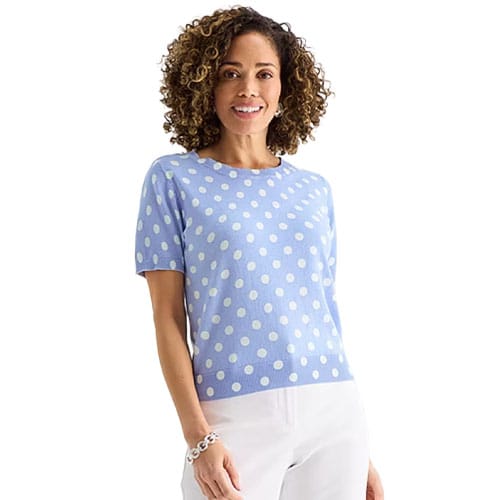 A woman wearing a light blue short-sleeve sweater with white polka dots, paired with white pants.