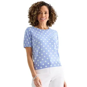 A woman wearing a light blue short-sleeve sweater with white polka dots, paired with white pants.