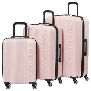 A set of three pink Calvin Klein hard-shell suitcases with black handles and wheels, each differing in size, featuring vertical grooves and the brand name embossed on the front.