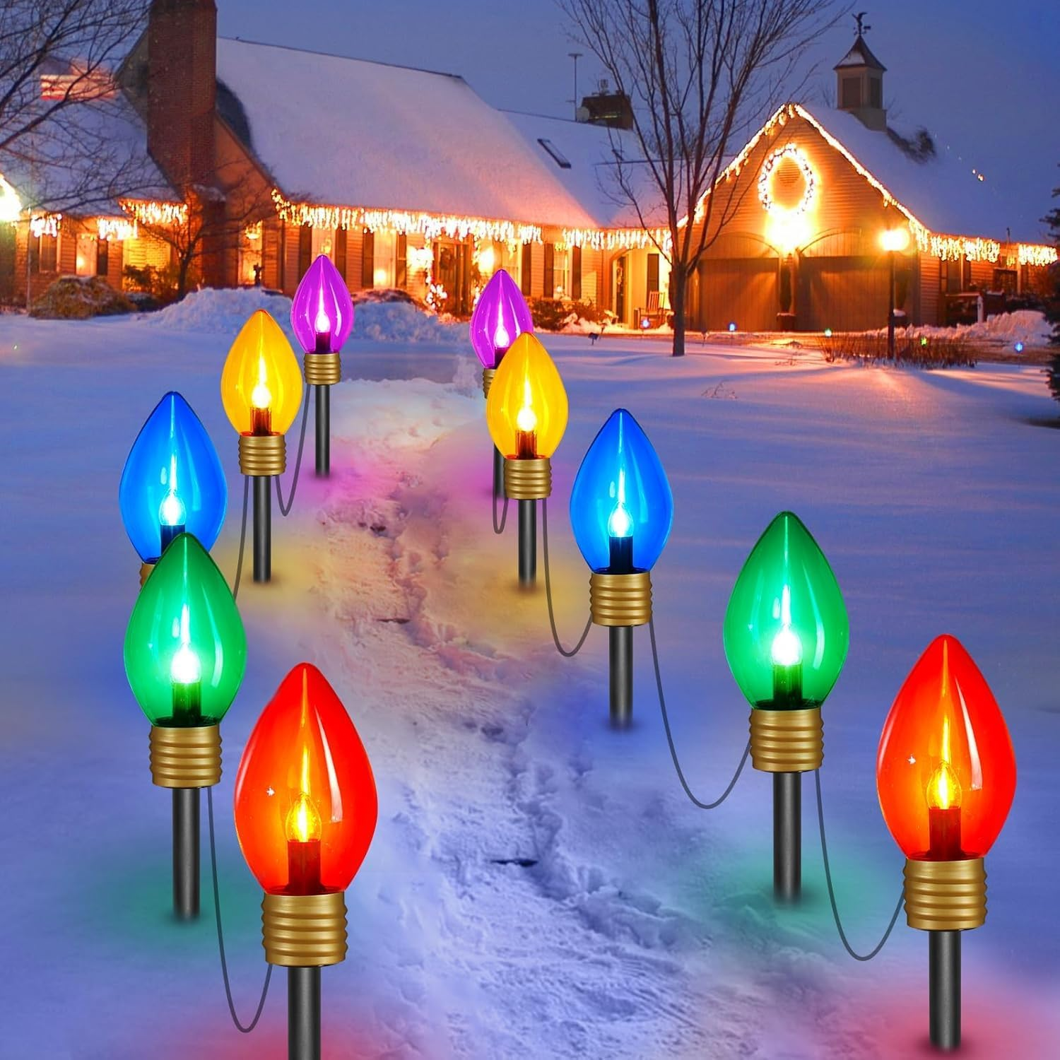 A snowy path is lined with large, colorful, bulb-shaped lights in red, blue, green, yellow, and purple, leading to a house decorated with Christmas lights.