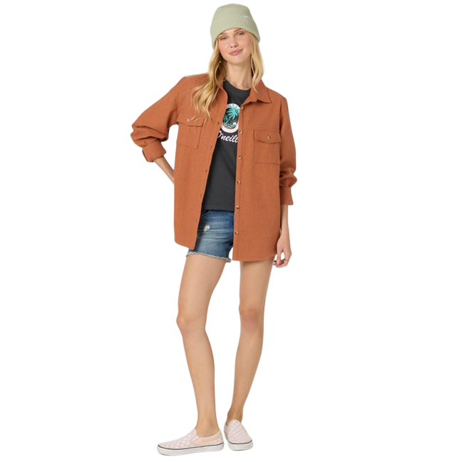 A woman is wearing a brown button-up shacket over a graphic t-shirt with denim shorts, paired with pink checkered slip-on sneakers and a light green beanie.