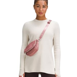 A person is wearing a light-colored, long-sleeve sweater and a crossbody bag in a pink shade.
