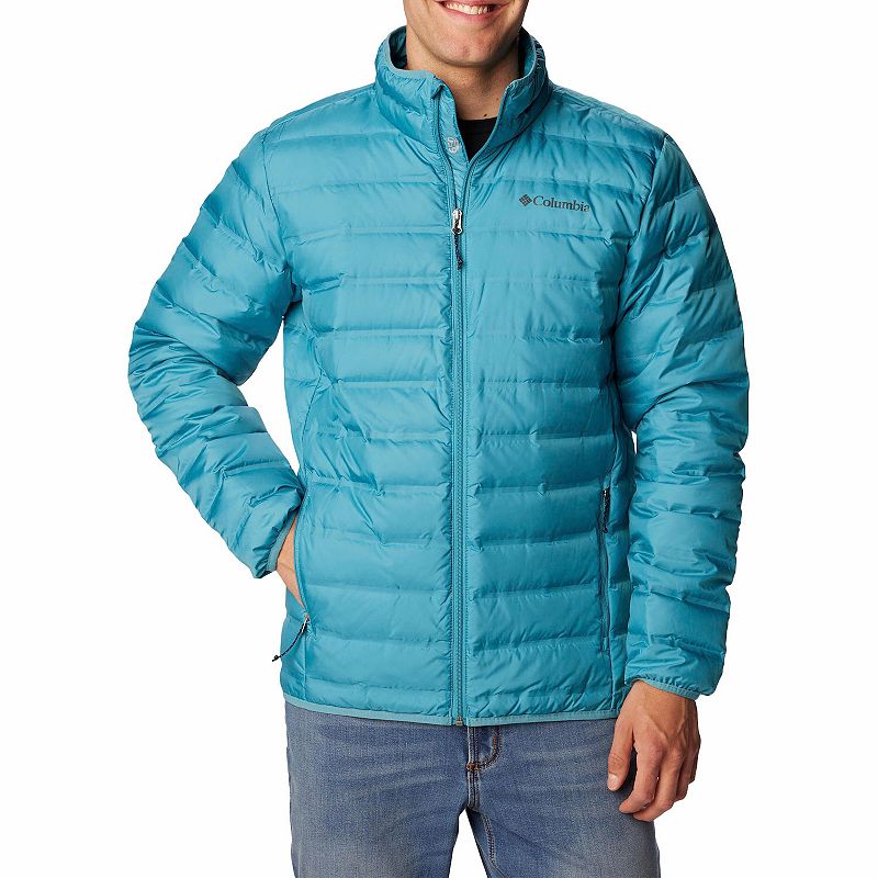 A man is wearing a blue, quilted Columbia Lake 22 Down Jacket with a zippered front, stand-up collar, and the Columbia logo on the left chest.