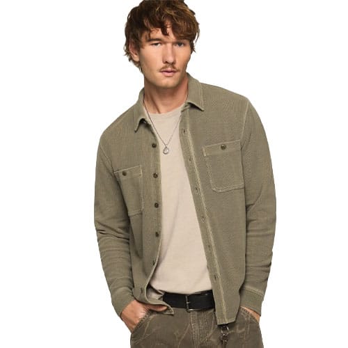 A man is wearing a textured button-up olive shirt over a beige t-shirt, paired with khaki pants and a black belt. A pendant necklace completes the outfit.