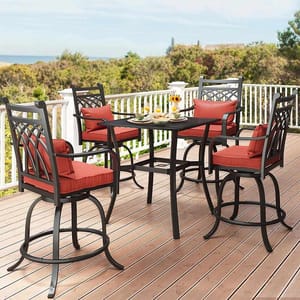 A patio set featuring a square table and four swivel chairs with dark metal frames and red cushions, situated on a wooden deck overlooking greenery and ocean.