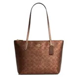 A brown Coach tote bag with signature C pattern, gold-tone hardware, and long straps, featuring a tag and zippered top closure.