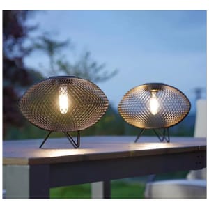 Two spherical wire mesh table lamps with interior light bulbs, set on an outdoor table during dusk.