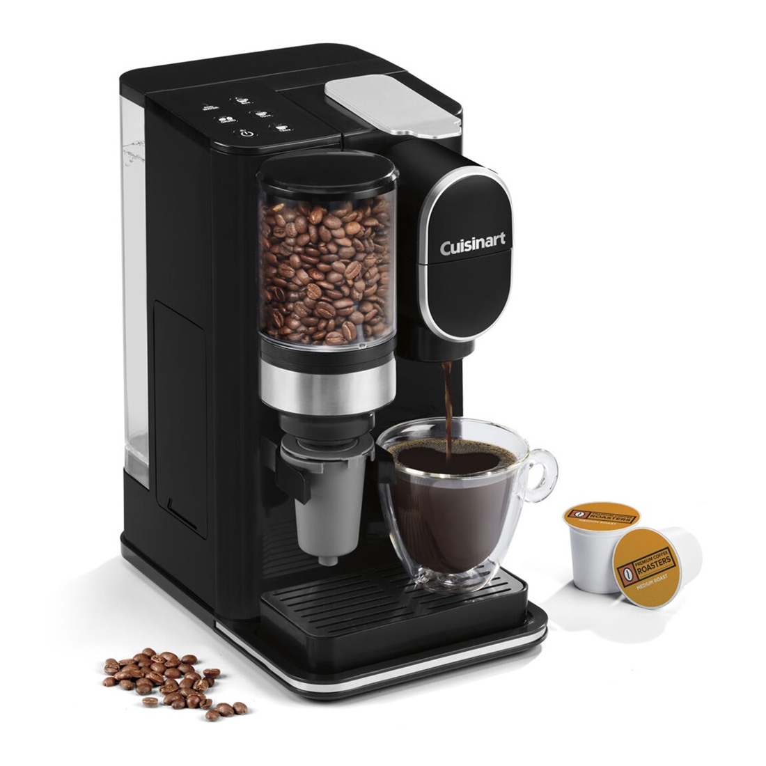 A black Cuisinart coffee maker with a built-in grinder holds coffee beans and brews coffee into a glass mug. Two K-Cup pods are placed beside it.
