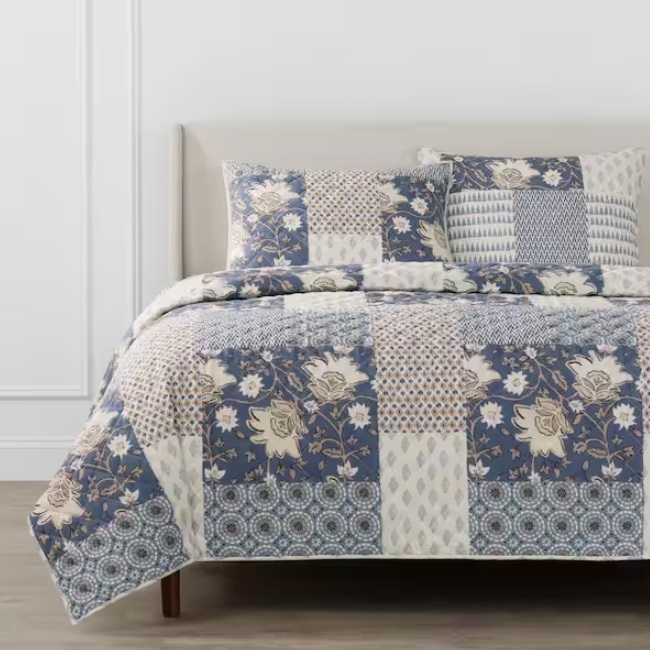 A bed covered with a patchwork quilt and matching pillows in various blue and white patterns.