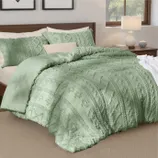 A green textured comforter set with pillows on a bed, featuring a detailed floral and geometric design. The setting includes a wooden bed frame, a bedside lamp, and a window with a view of trees.