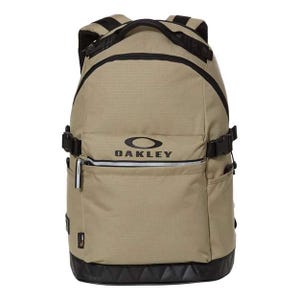 Tan Oakley backpack with black accents, featuring a front zippered pocket, side pockets, adjustable straps, and a reinforced base.
