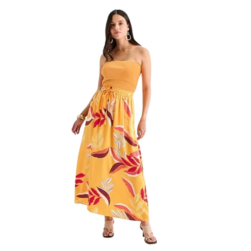A woman is wearing a strapless yellow maxi dress with a colorful floral pattern and accessorized with hoop earrings and brown sandals.