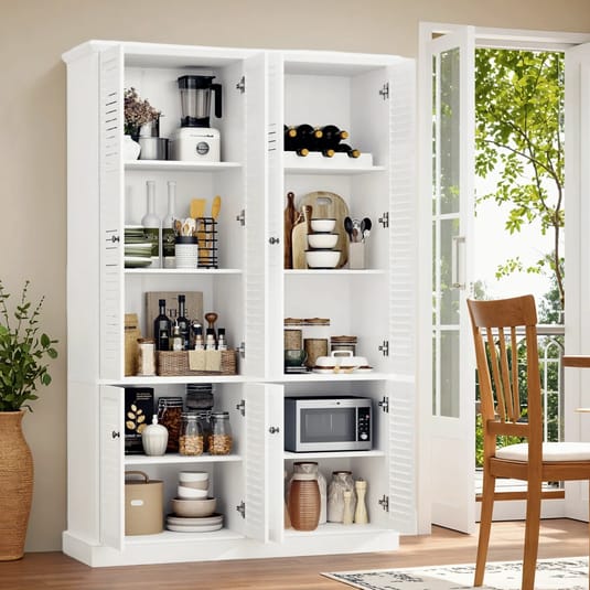 A white kitchen cabinet with open doors revealing shelves holding kitchen appliances, wine bottles, cutting boards, bowls, jars, a microwave, and pantry items, next to an open patio door.