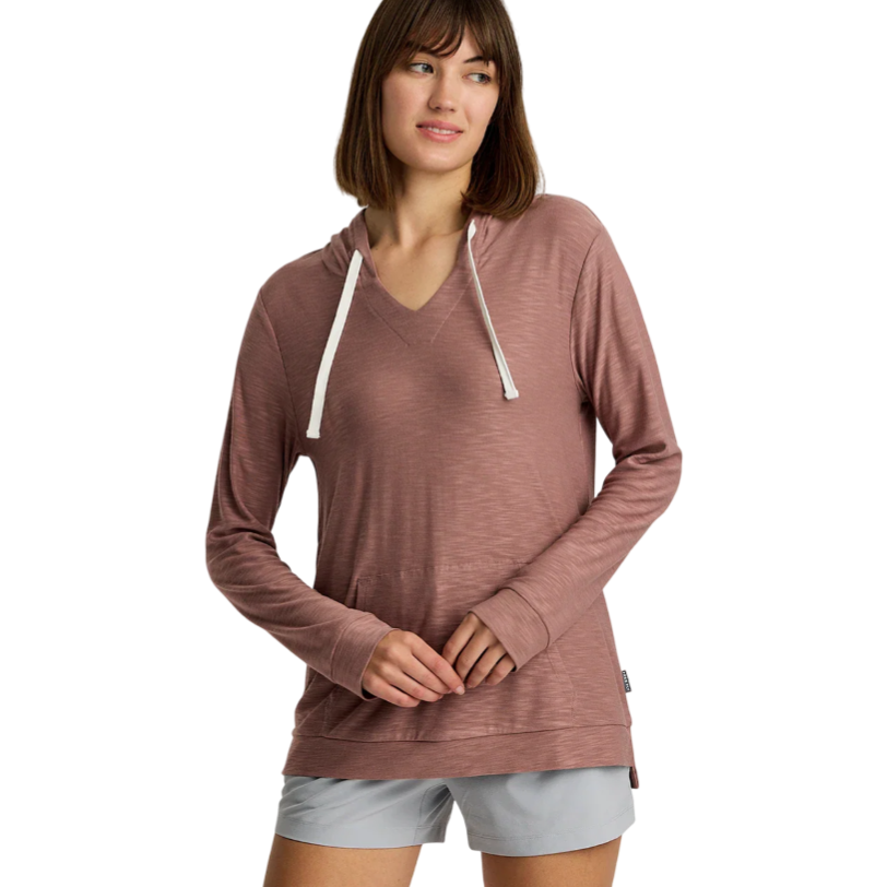 A woman is wearing a mauve long-sleeve hooded pullover with a V-neck and drawstrings, paired with light gray shorts.