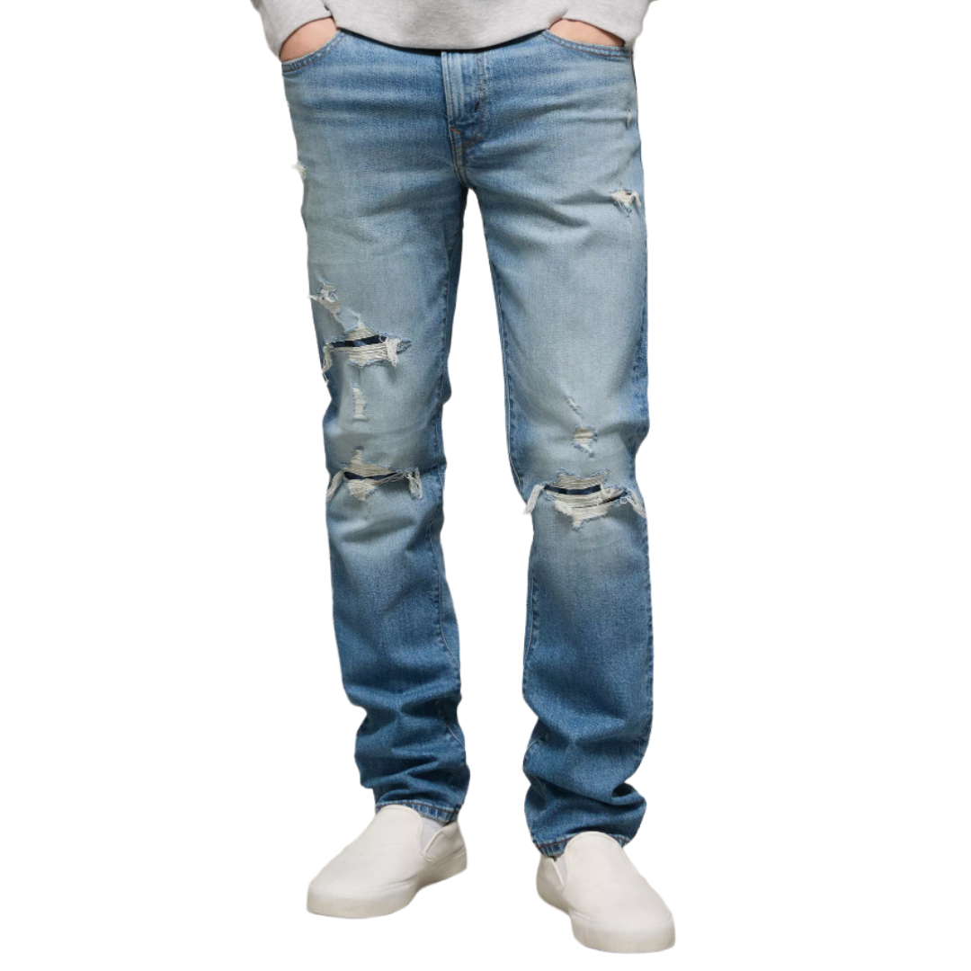 Light blue distressed jeans with rips and a straight fit, paired with white slip-on shoes.