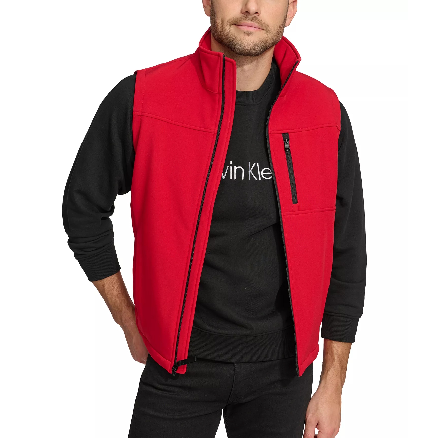 A man is wearing a red sleeveless vest with a black zippered pocket over a black Calvin Klein sweatshirt, paired with black jeans.