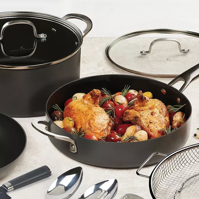 Kitchen cookware, including a black roasting pan with chicken, a pot with a lid, a frying pan, and cooking utensils.
