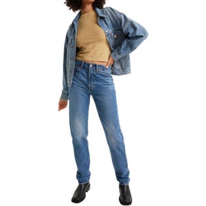 A person is wearing a denim jacket over a beige shirt, paired with blue jeans and black ankle boots.