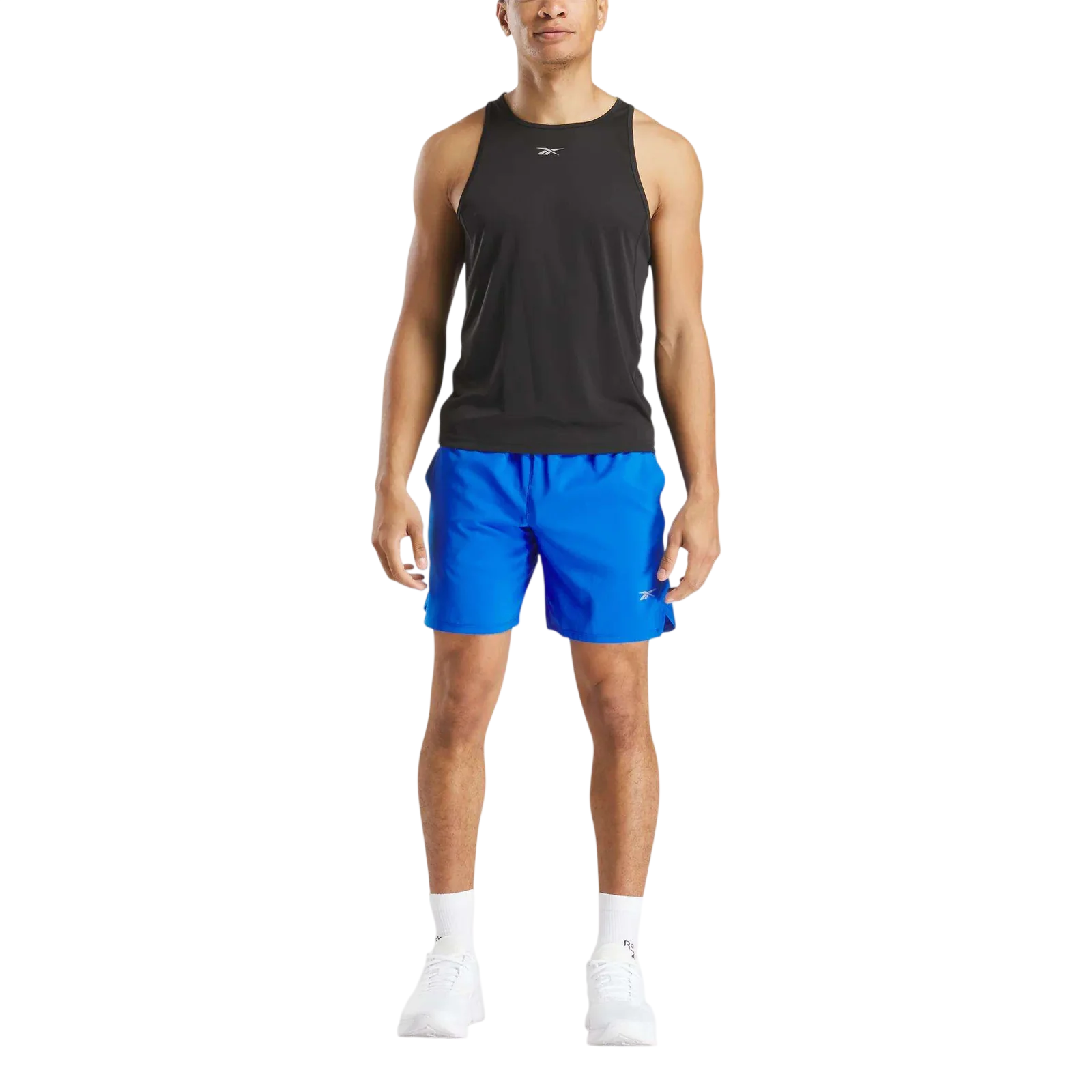 A man is wearing a black tank top, blue athletic shorts, and white sneakers with socks. Both the tank top and shorts feature a small logo.