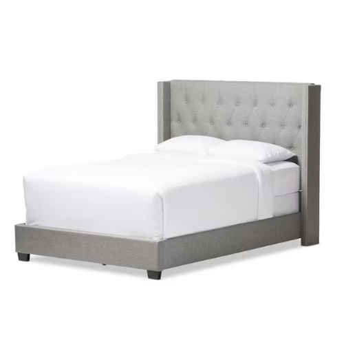 A gray upholstered bed with a high, tufted headboard and low-profile base, featuring nailhead trim accents along the sides.