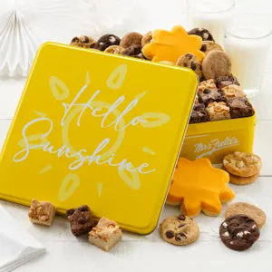 Yellow tin labeled \“Hello Sunshine\“ with assorted cookies and brownies, including chocolate chip, sugar cookies, and brownie squares. Two glasses of milk in the background.