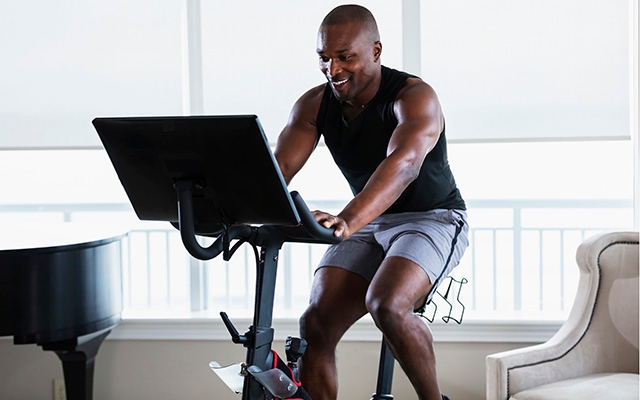 A man is using a stationary exercise bike with a large screen attached.