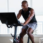 A man is using a stationary exercise bike with a large screen attached.