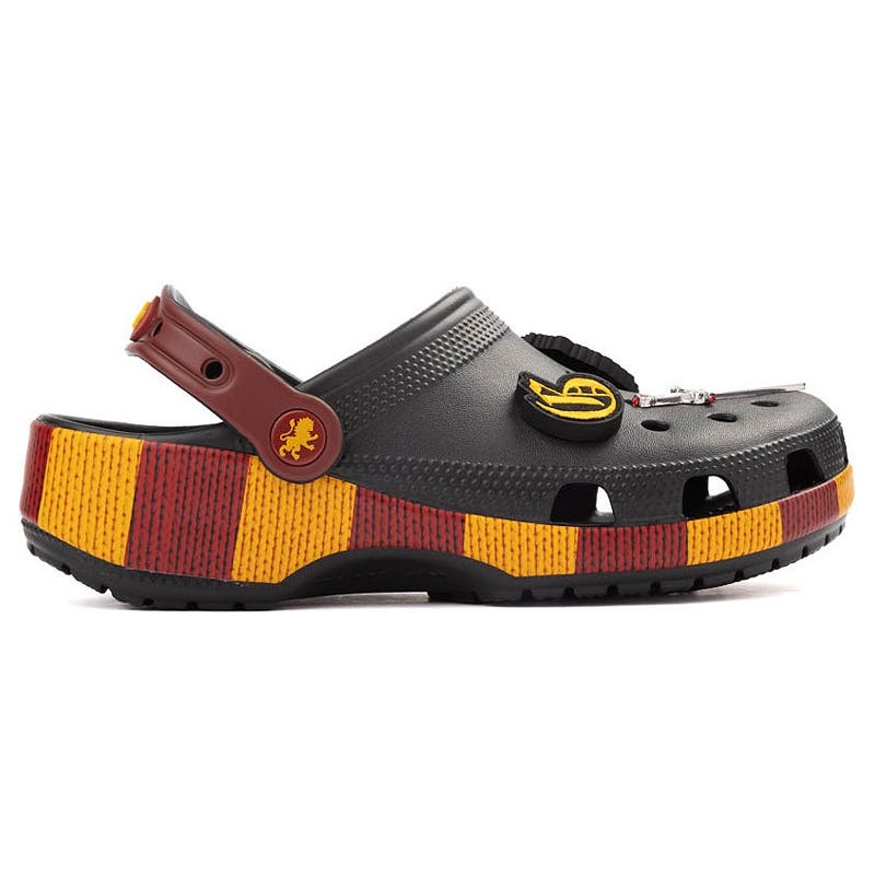 A grey clog with a colorful striped platform in red and yellow, featuring themed embellishments like a lion emblem on the strap and additional decorative charms on the upper section.