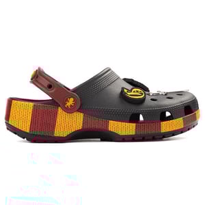 A grey clog with a colorful striped platform in red and yellow, featuring themed embellishments like a lion emblem on the strap and additional decorative charms on the upper section.