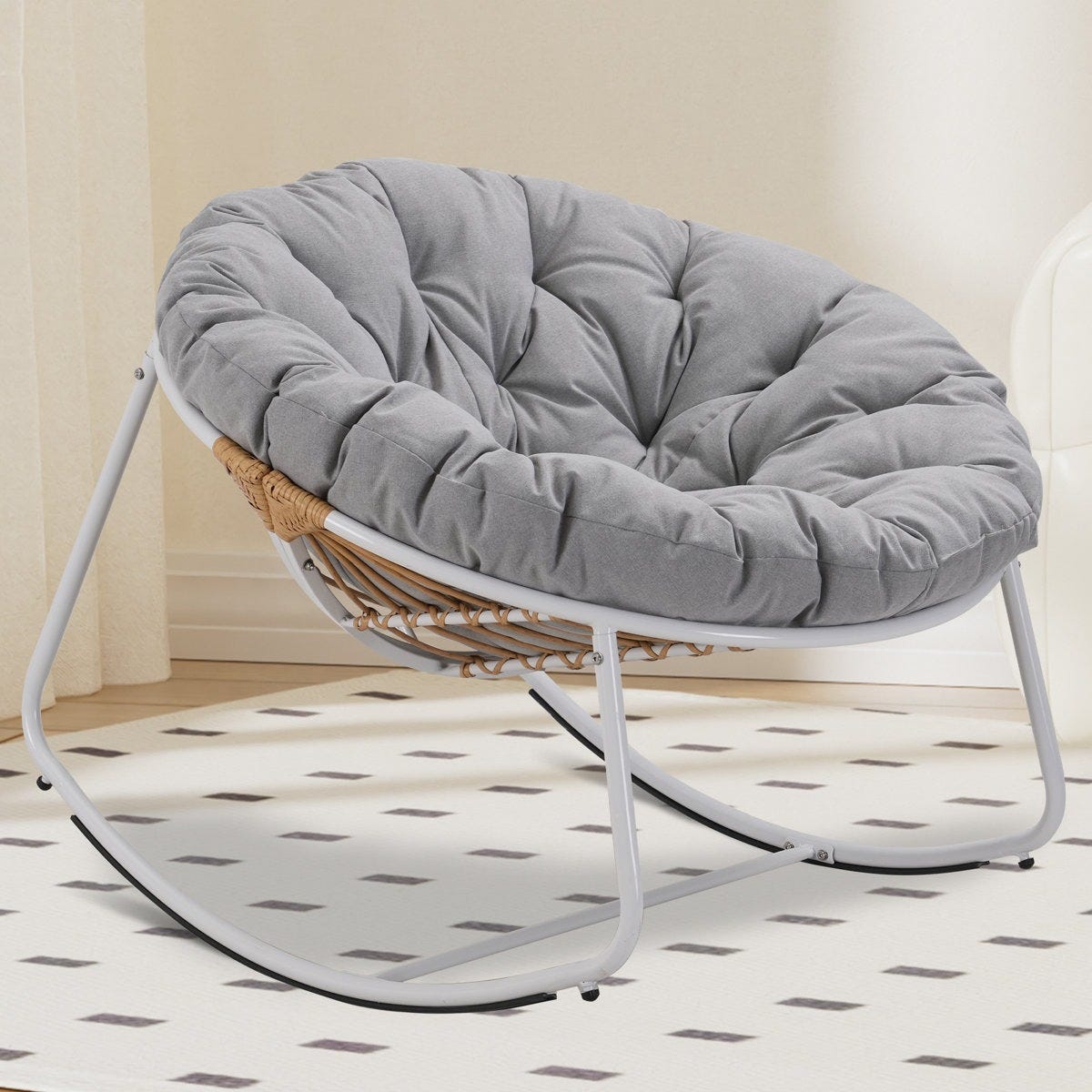 Round cushioned chair with a gray, tufted cushion, featuring a white metal frame and wicker accents. Designed for indoor spaces, it offers a casual, comfortable seating option.