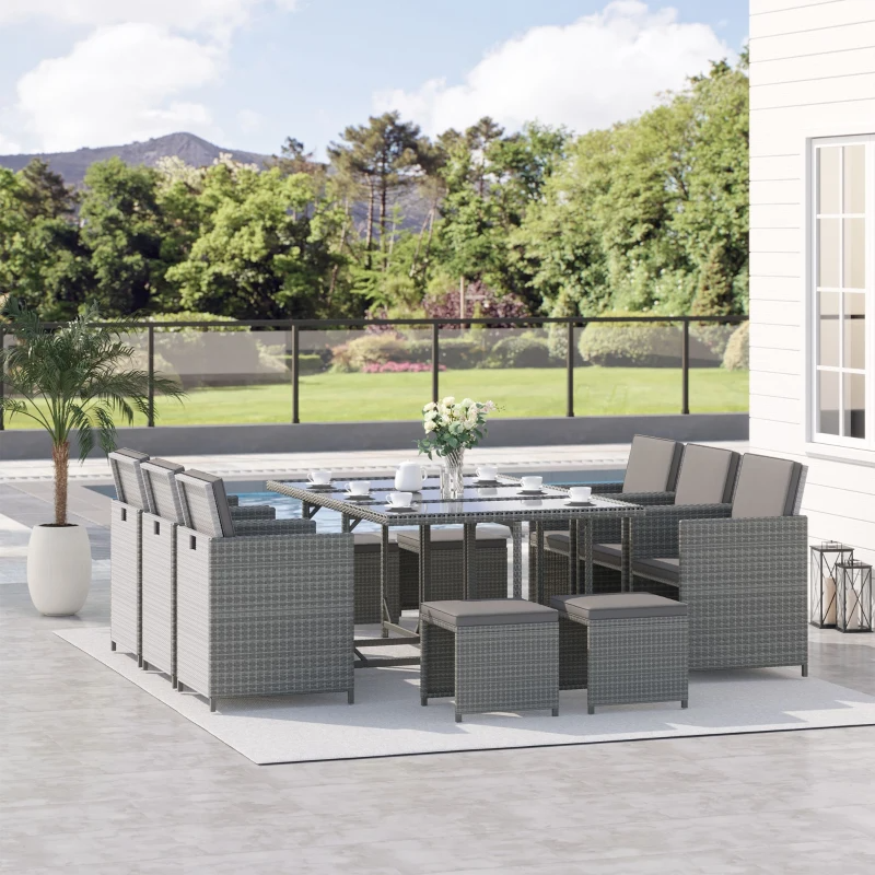 Outdoor patio set with a rectangular glass-top table, cushioned chairs, and matching ottomans in a wicker design, set against a backdrop of greenery and a pool.