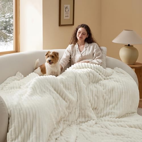 A white, plush blanket covers a woman and her dog on a curved sofa in a cozy room with a table lamp and wall art.