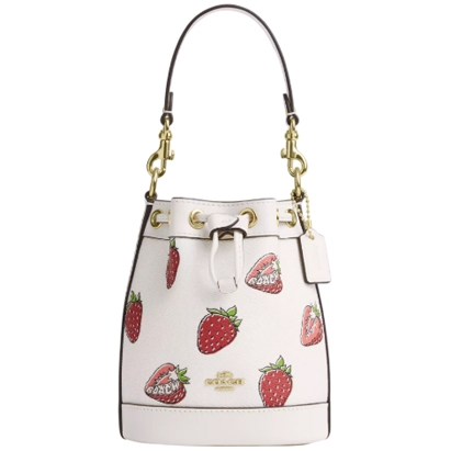 A white Coach Outlet bucket bag with a drawstring closure and gold hardware, featuring a playful strawberry print.