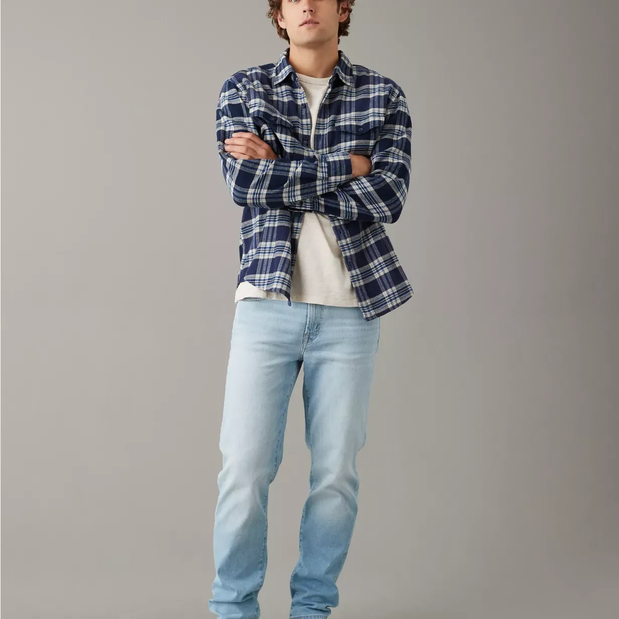 A man wearing a blue and white plaid shirt, white t-shirt, light blue jeans, and white sneakers.