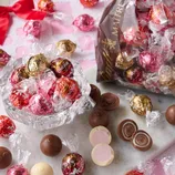 A variety of Lindt Lindor chocolate truffles are displayed, including red, pink, and gold-wrapped chocolates, some of which are cut open to show their creamy centers.