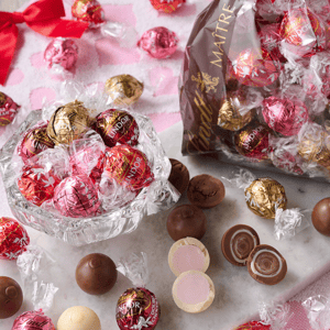 A variety of Lindt Lindor chocolate truffles are displayed, including red, pink, and gold-wrapped chocolates, some of which are cut open to show their creamy centers.