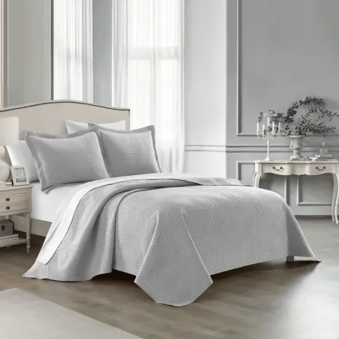 A gray, textured bedding set with a quilt and matching pillow shams in a neatly arranged, classic bedroom featuring an upholstered headboard, side table, and elegant decorative elements.